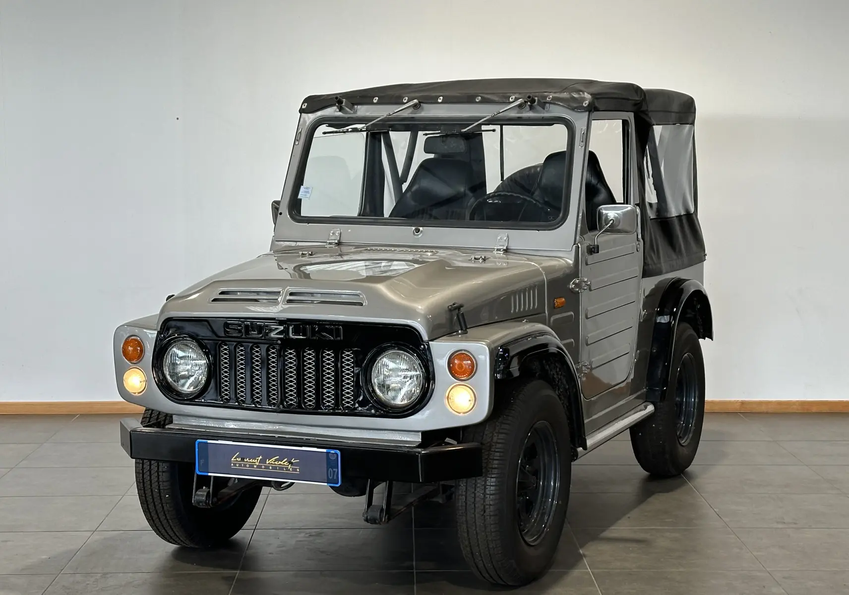 Suzuki Across LJ80 Cabriolet gris vu de trois quarts avant droit avec capote noire et phares allumés.