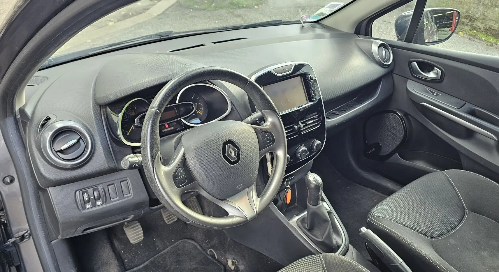 Intérieur côté conducteur de la Renault Clio IV grise, montrant le volant, tableau de bord et console centrale avec écran tactile.