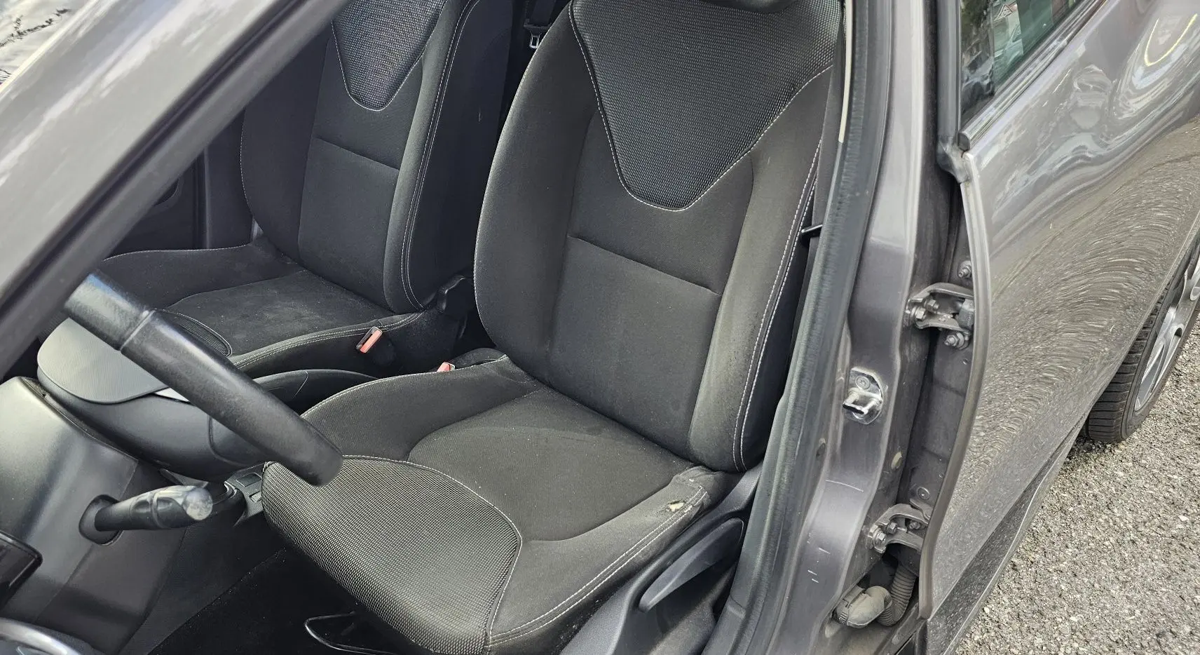Vue intérieure côté conducteur de la Renault Clio IV grise de 2015, montrant les sièges en tissu noir et le volant.