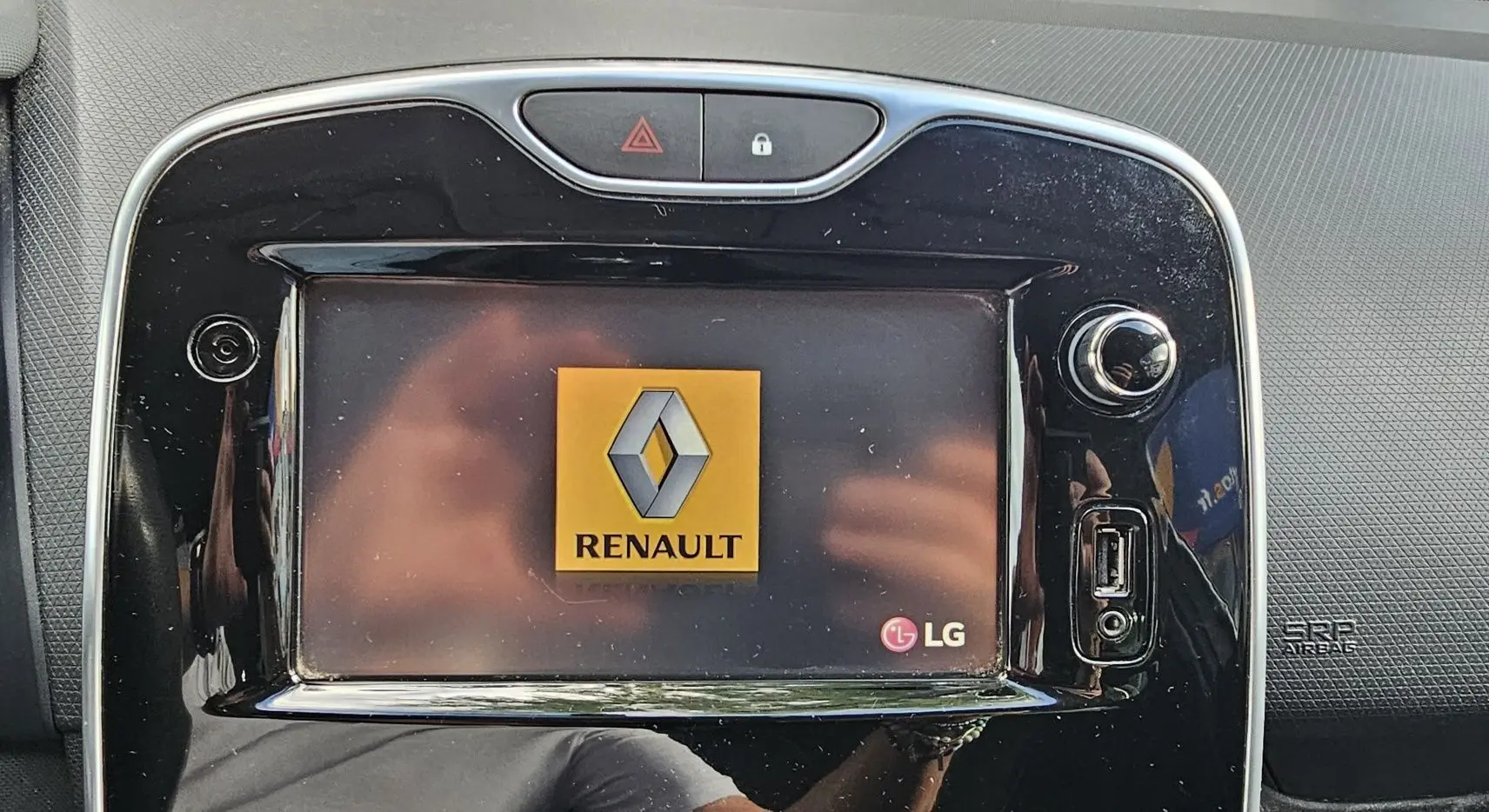 Écran tactile central LG affichant le logo Renault dans l'habitacle d'une Clio IV gris 2015, finition Zen.