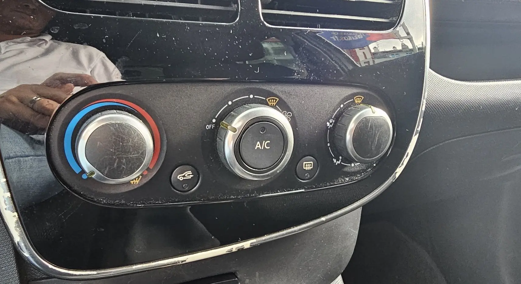 Commandes de climatisation avec réglages manuels et bouton A/C sur le tableau de bord noir d'une Renault Clio IV grise.
