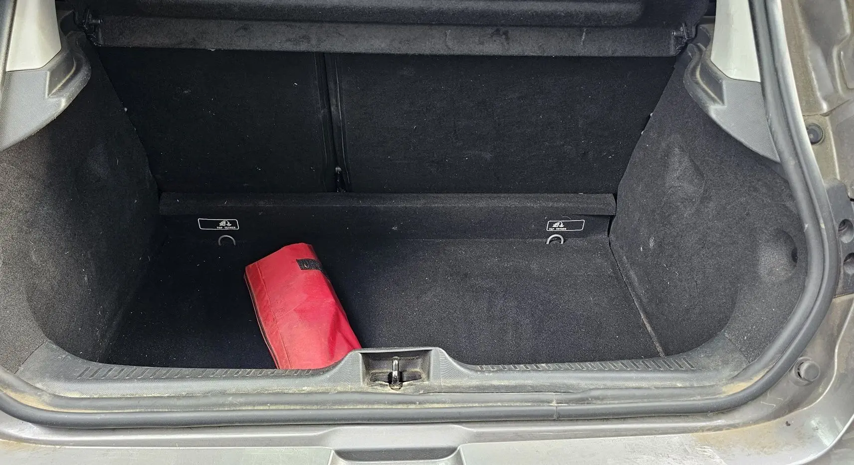 Coffre ouvert d’une Renault Clio IV grise de 2015, montrant un sac rouge à l’intérieur et la garniture noire du coffre.
