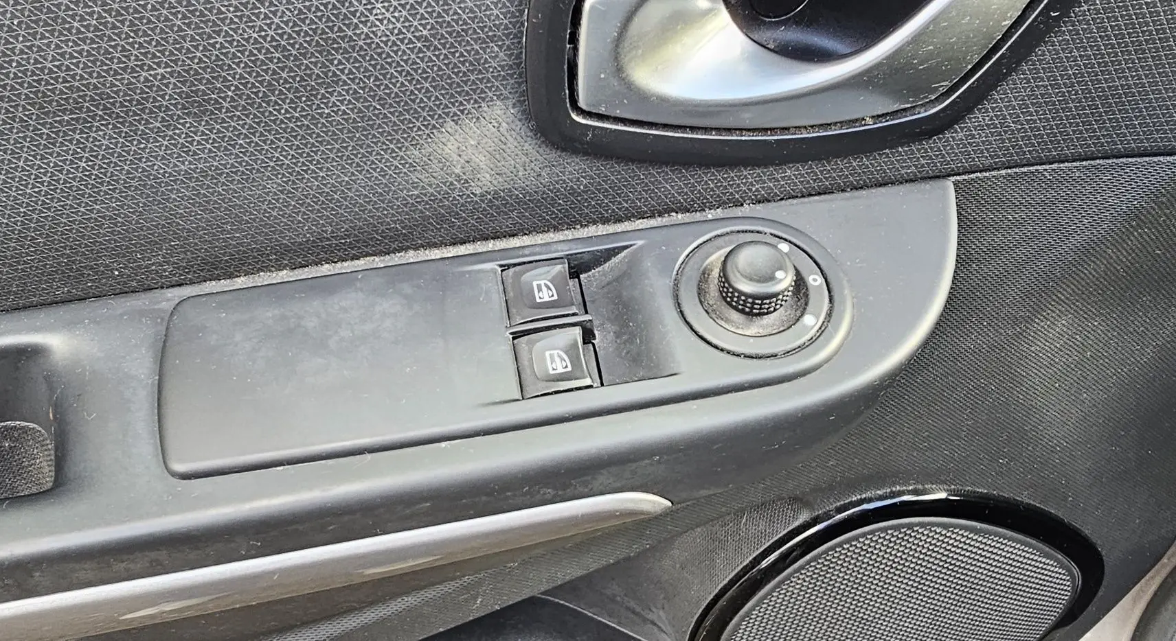 Gros plan sur la commande des vitres électriques et le réglage des rétroviseurs côté conducteur d'une Renault Clio IV grise.
