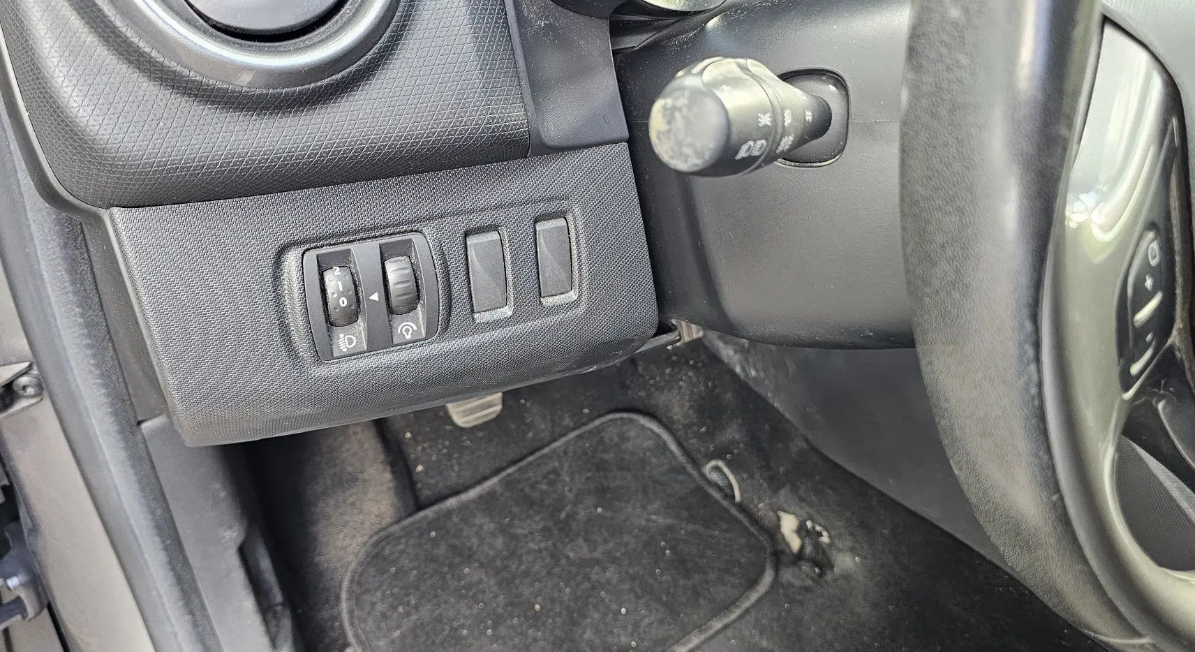 Vue rapprochée du tableau de bord côté gauche d'une Renault Clio IV grise, montrant les commandes d'éclairage et le volant.