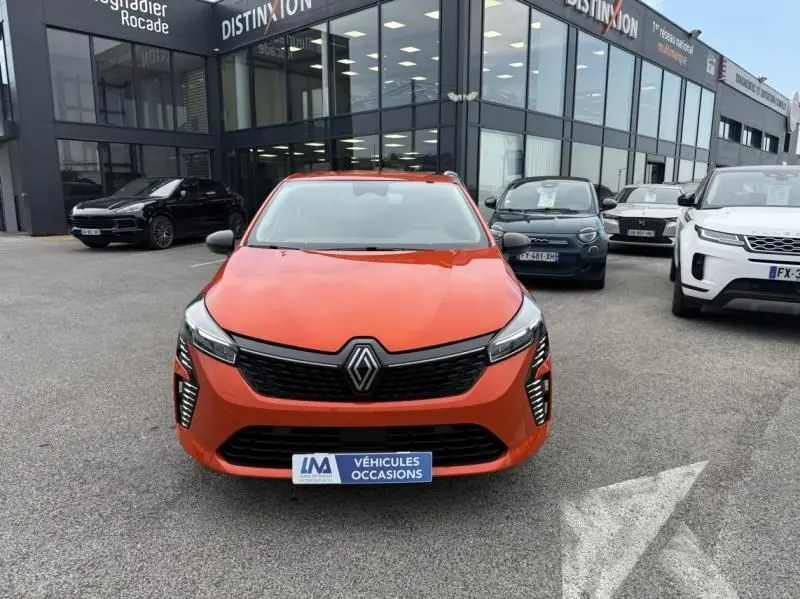 Vue de face d'une Renault Clio V SCE 65 Evolution orange vif, avec calandre noire et feux LED verticaux allumés.