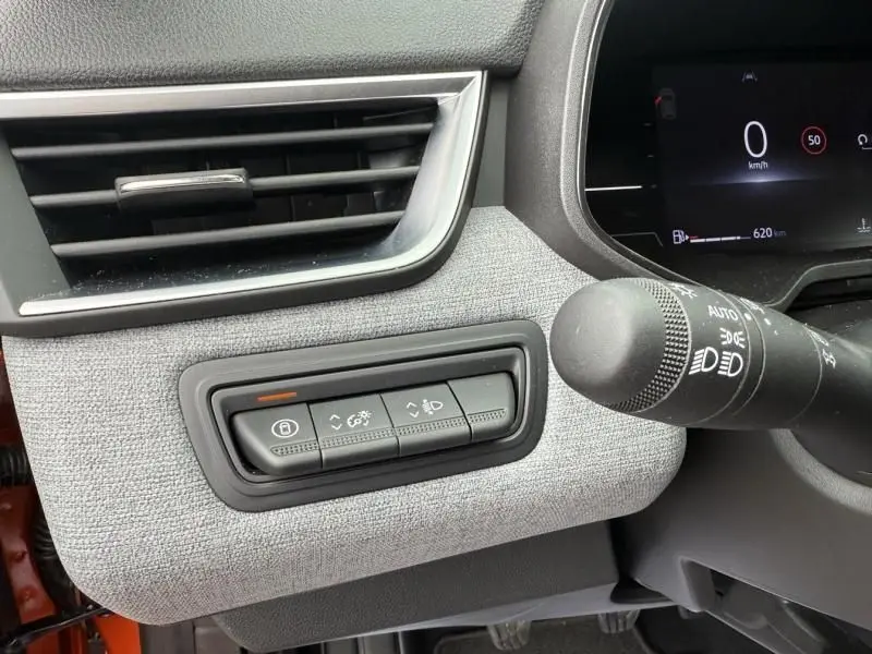 Détail du tableau de bord gris clair de la Renault Clio V orange, avec commandes d’éclairage et ventilation visibles.