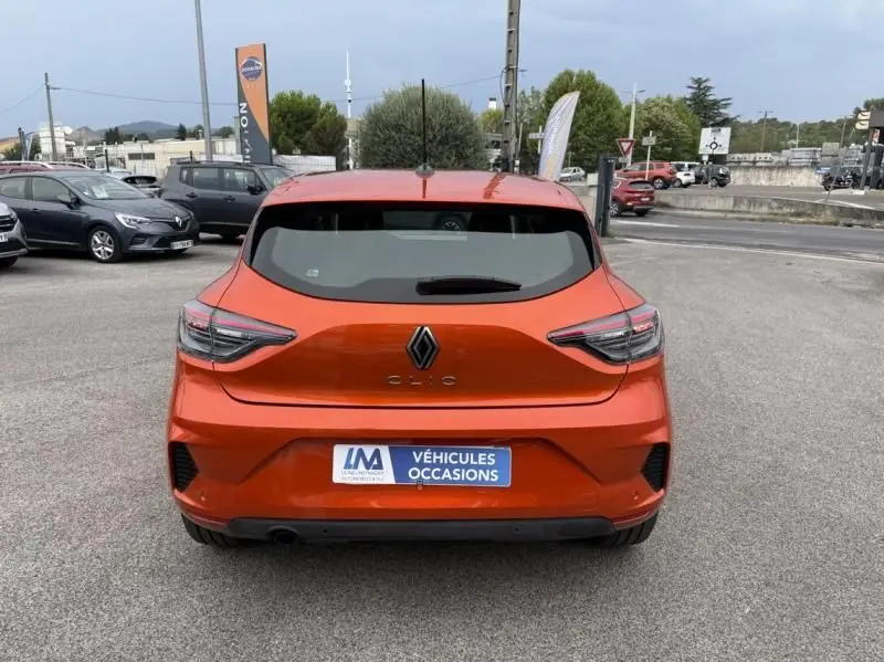 Vue arrière d'une Renault Clio V orange 2025 avec feux LED et plaque d'occasion sur un parking extérieur.