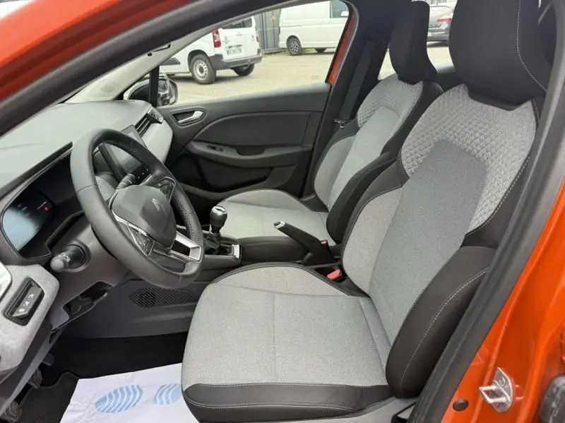 Intérieur de la Renault Clio V SCE 65 Evolution 2025, vue côté conducteur, sièges gris et orange extérieur visible.