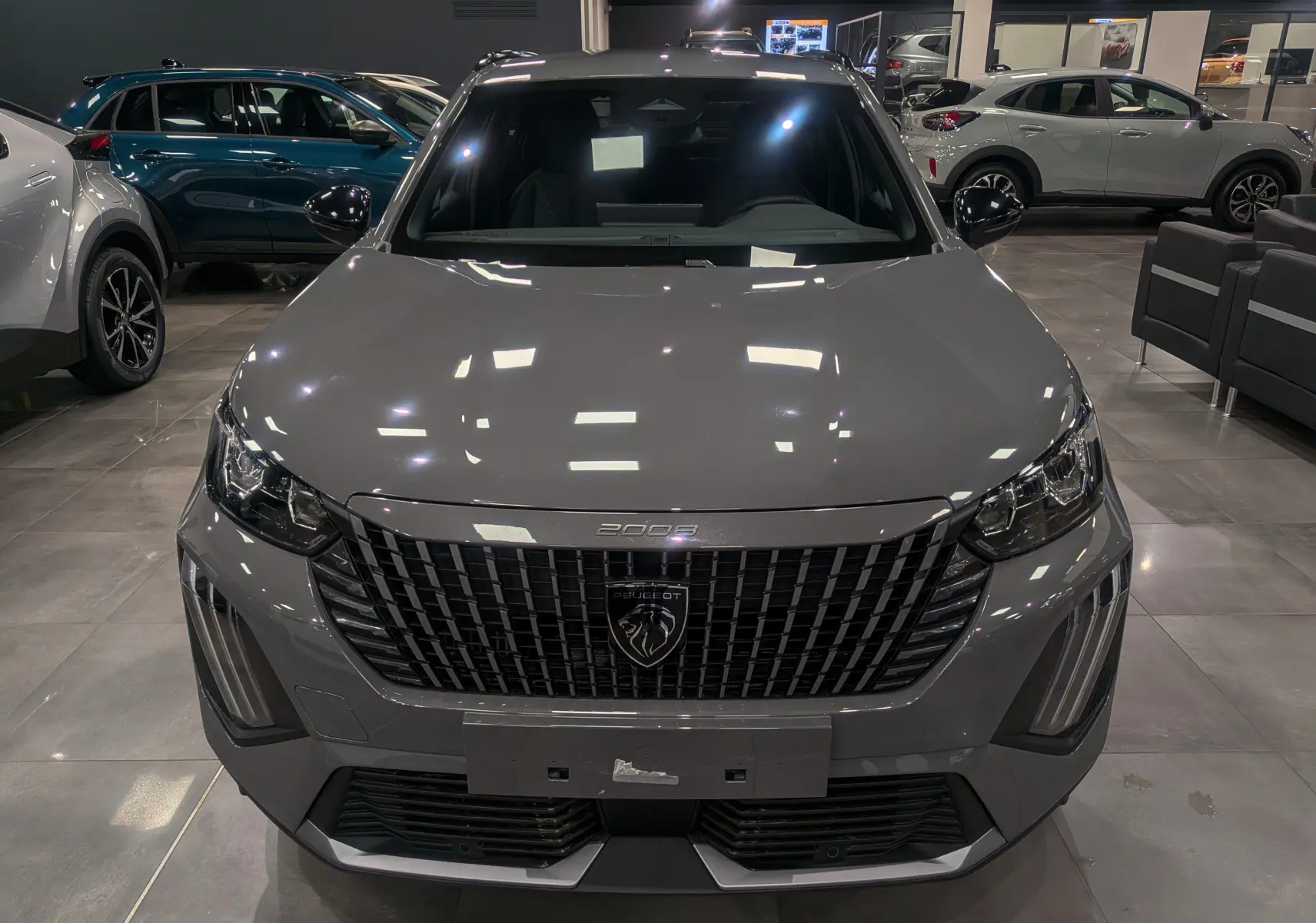 Vue frontale d'un Peugeot 2008 Hybrid 145 gris Sélénium avec calandre noire et éclairage LED en showroom.