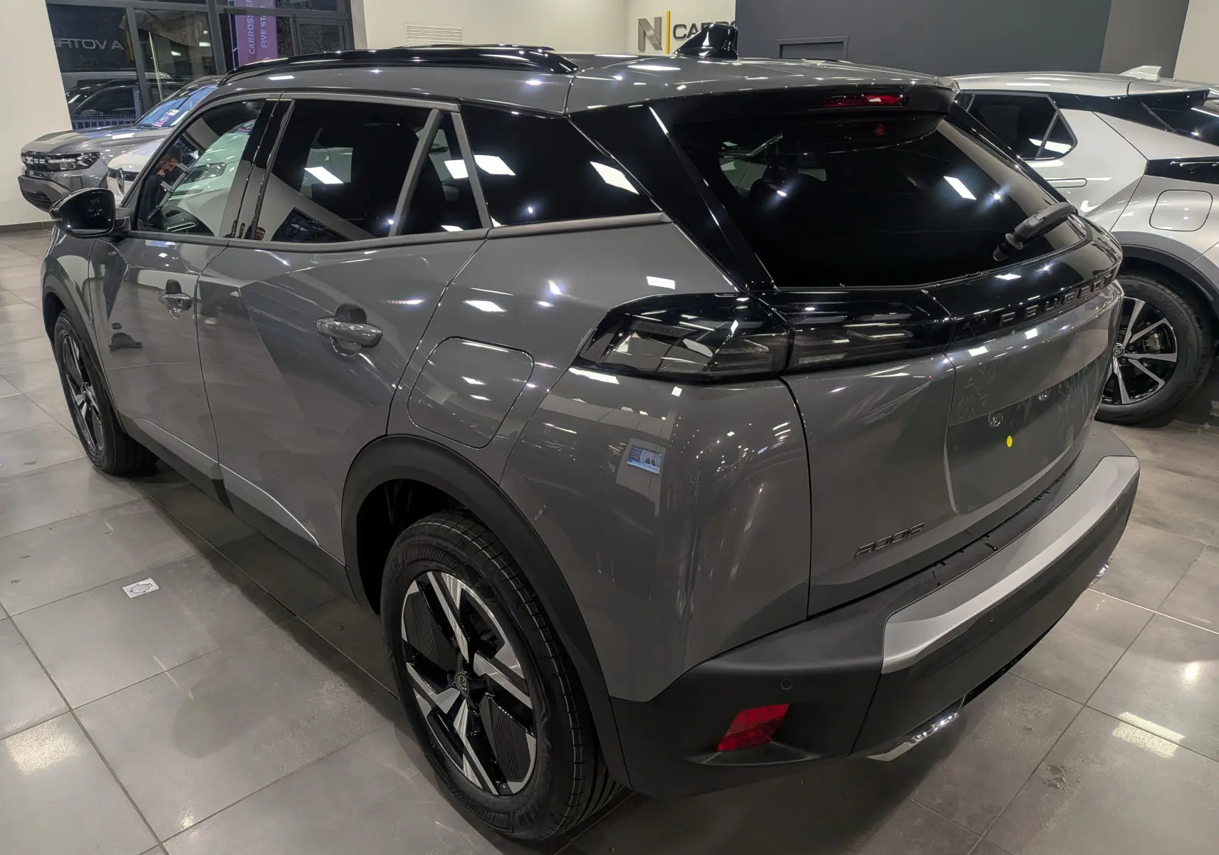Peugeot 2008 Hybrid 145 gris Sélénium vue 3/4 arrière droit avec toit noir brillant en showroom.