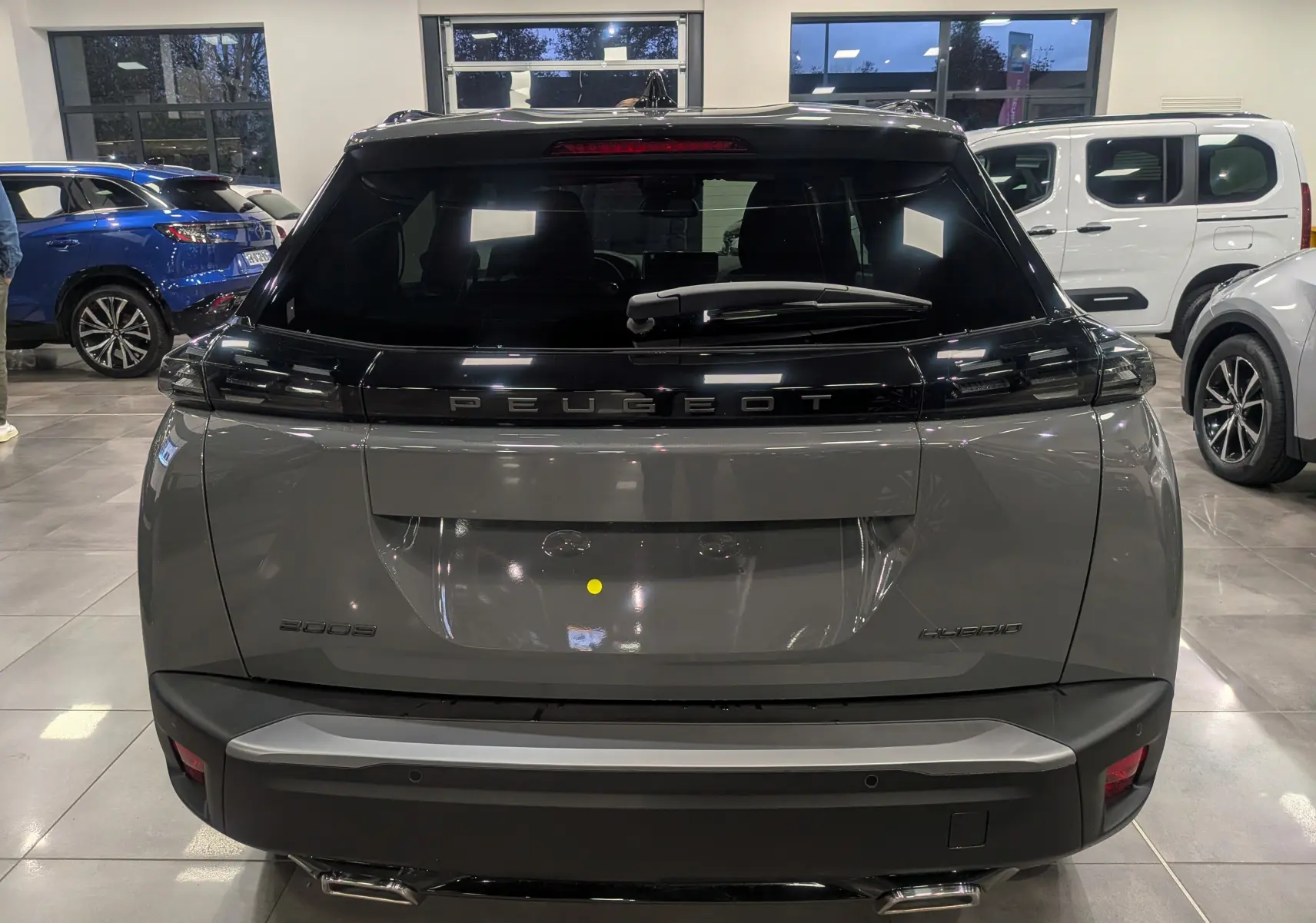Vue arrière d'un Peugeot 2008 Hybrid 145 e-DCS6 Allure gris Sélénium dans un showroom lumineux.