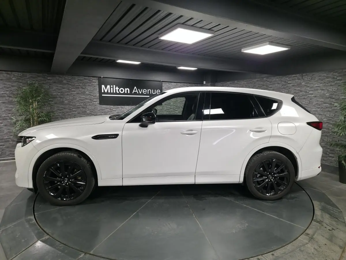 Vue de profil côté gauche du Mazda CX-60 blanc Arctic White avec jantes alliage noires dans un showroom.