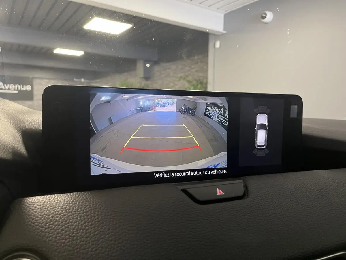 Écran central affichant la caméra de recul et la vue 360° du Mazda CX-60 blanc en stationnement intérieur.