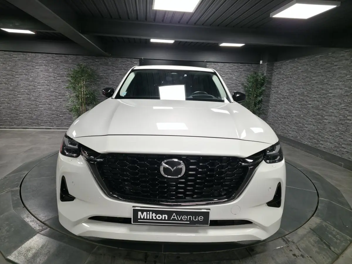 Vue frontale d'un Mazda CX-60 blanc avec calandre noire brillante et phares LED dans un showroom.
