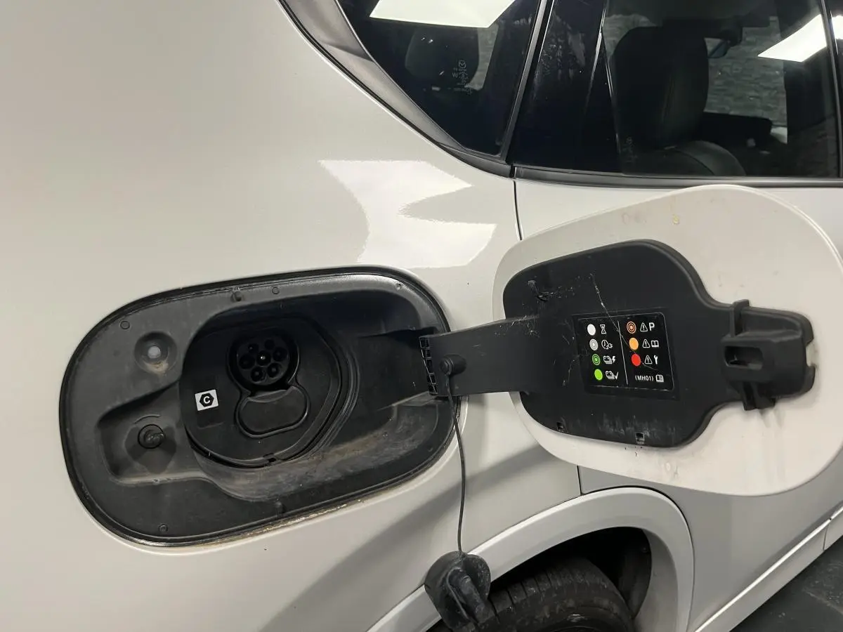 Prise de recharge ouverte côté gauche sur un Mazda CX-60 blanc hybride rechargeable, détail de la trappe et connecteur.