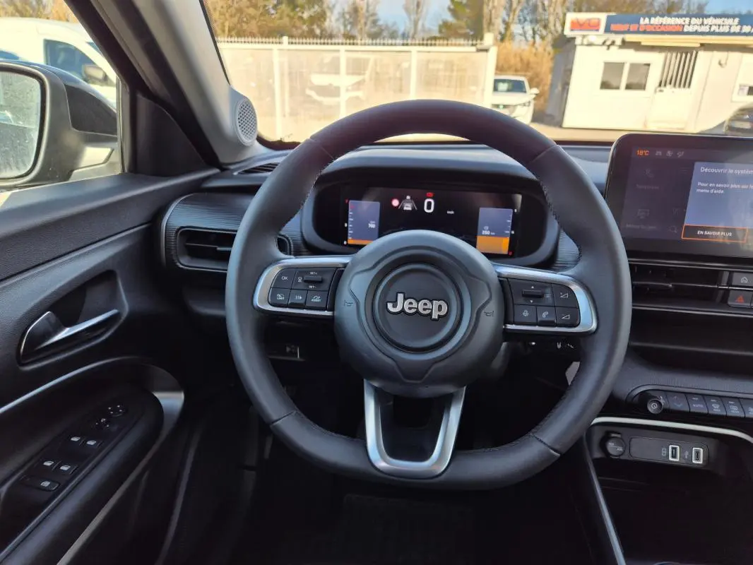 Vue intérieure centrée sur le volant Jeep noir avec tableau de bord numérique et écran tactile à droite.