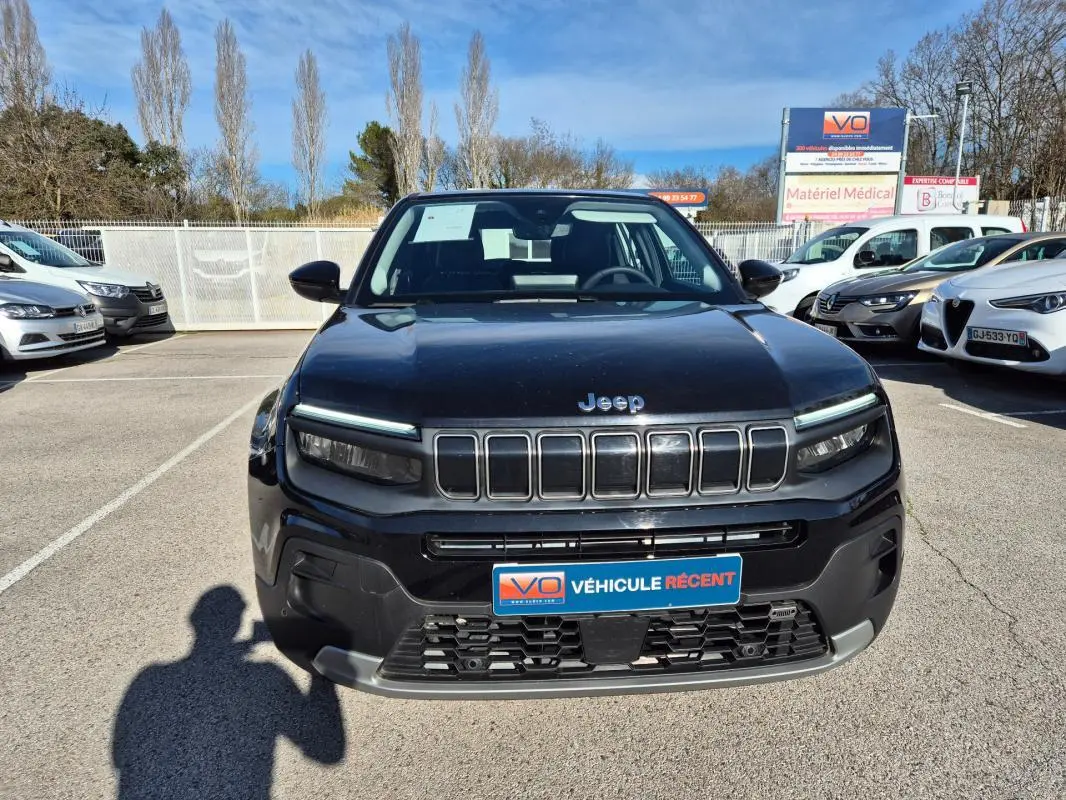 Vue avant d'un Jeep Avenger noir 2024 avec calandre distinctive et phares LED fins, sur parking extérieur.