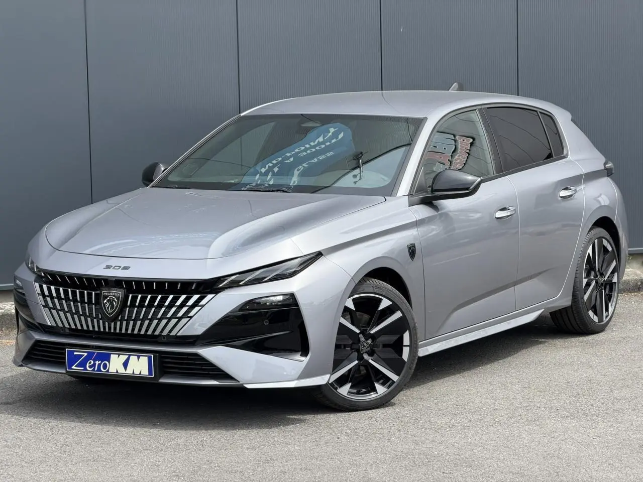 Peugeot 308 gris Artense en 3/4 avant droit, avec calandre distinctive et jantes alliage bi-tons.
