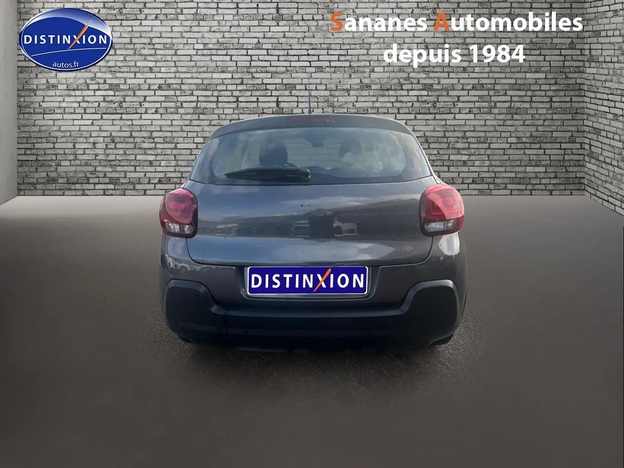 Vue arrière d'une Citroën C3 gris foncé 2023 avec feux rouges et pare-chocs noir mat sur sol gris.