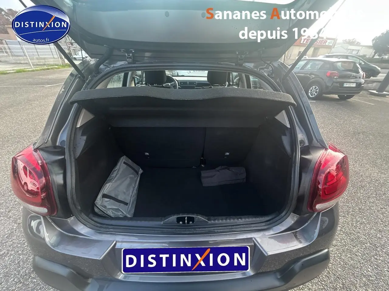 Coffre ouvert d'une Citroën C3 gris foncé vue arrière, avec intérieur de coffre vide et deux sacs posés.