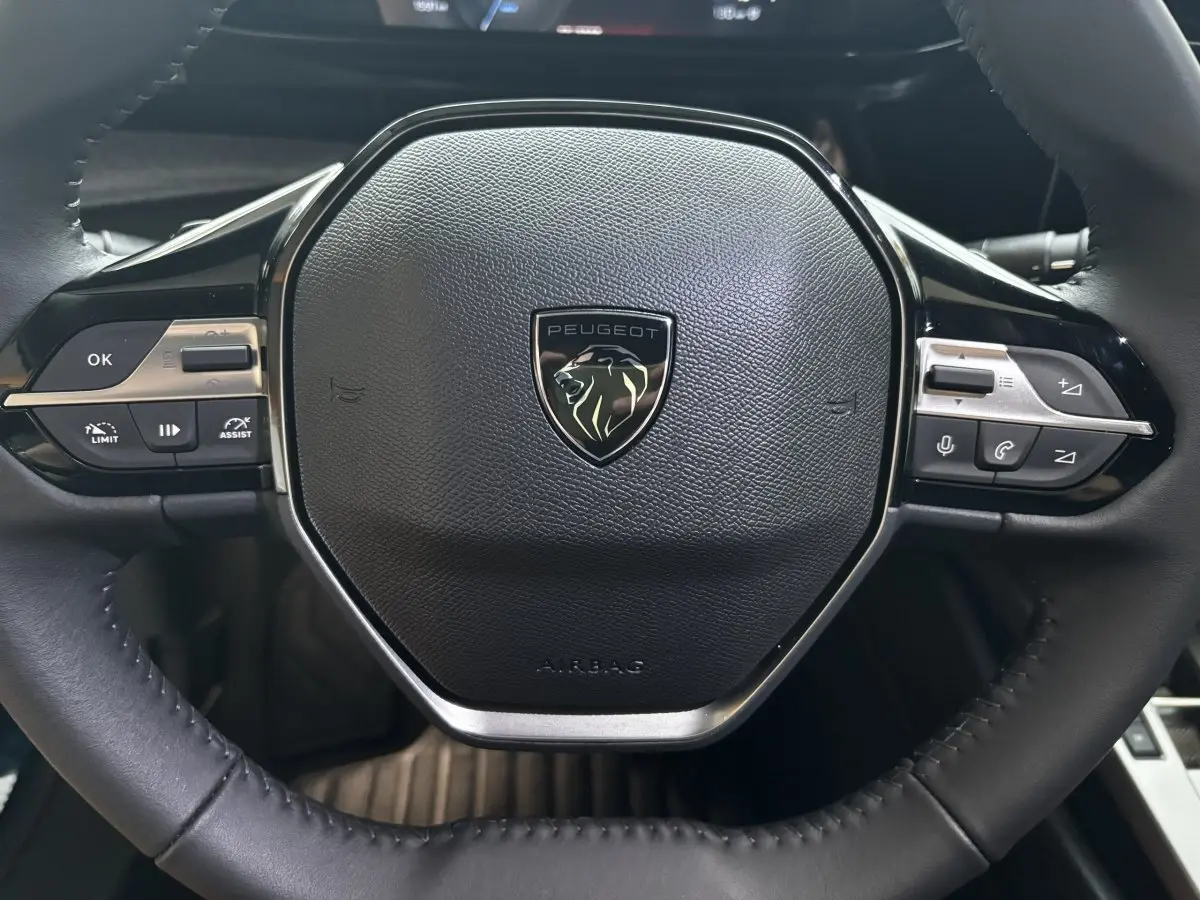 Gros plan sur le volant cuir noir multifonctions de la Peugeot 308 Hybrid 2025 avec logo lion central.