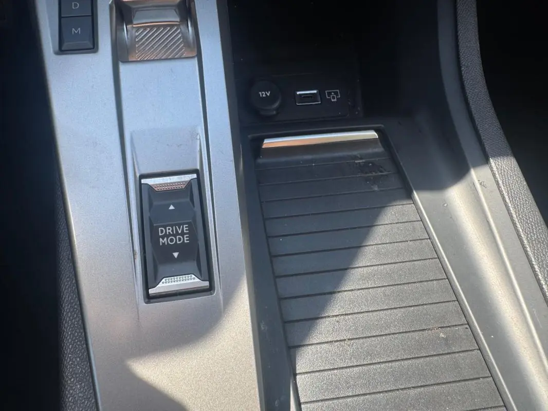 Gros plan sur la console centrale grise de la Peugeot 308 Hybrid 136 e-DCS6 Allure avec bouton Drive Mode et prise USB visible.