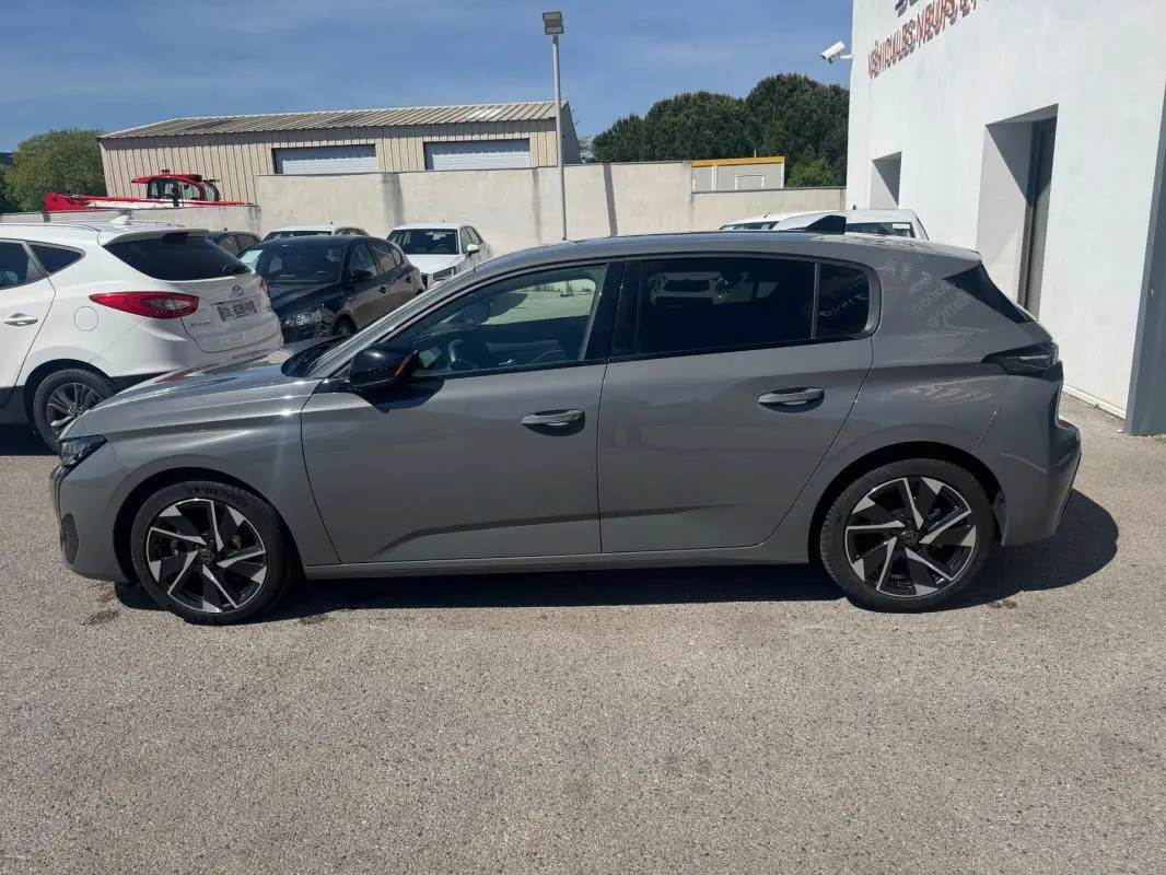 Profil côté gauche de la Peugeot 308 Hybrid gris 2025 avec jantes alliage 17 pouces, stationnée en extérieur.