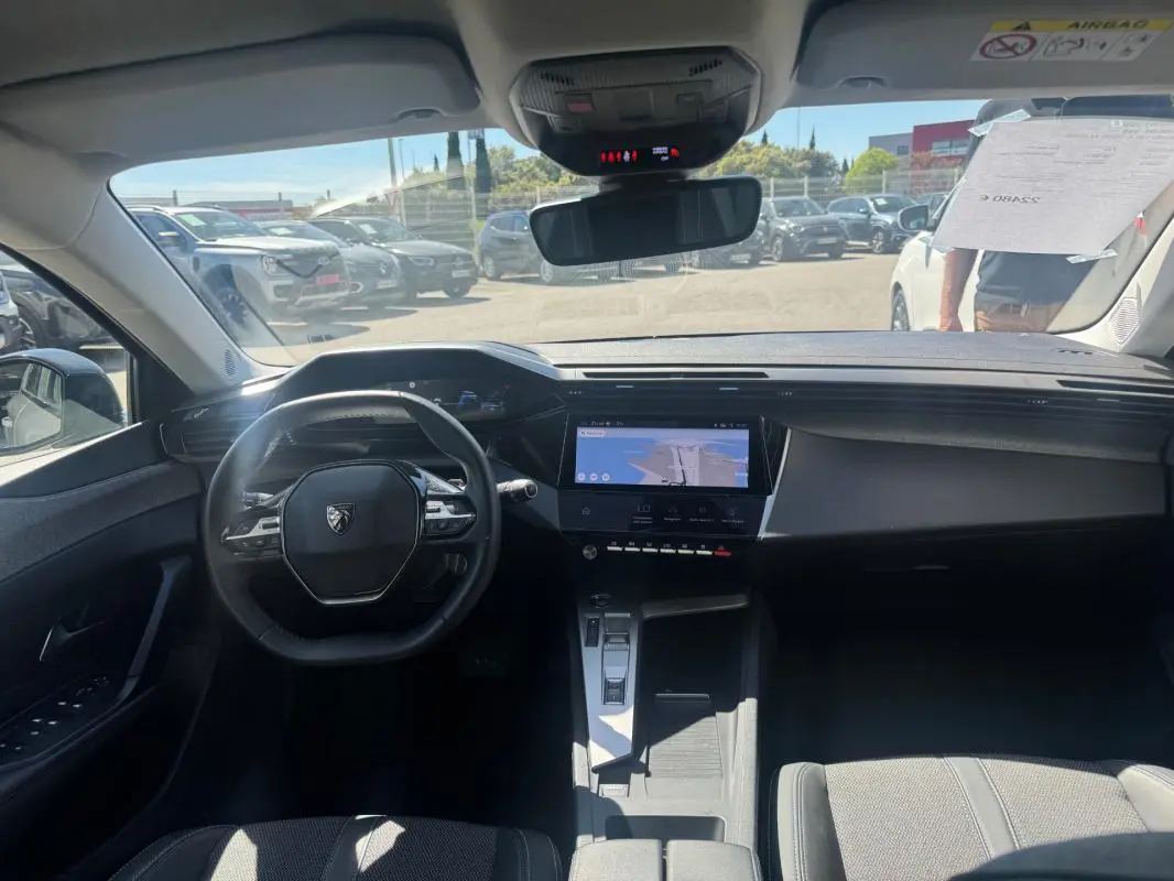 Vue intérieure avant de la Peugeot 308 Hybrid 136 e-DCS6 Allure gris, avec volant compact et écran tactile central lumineux.