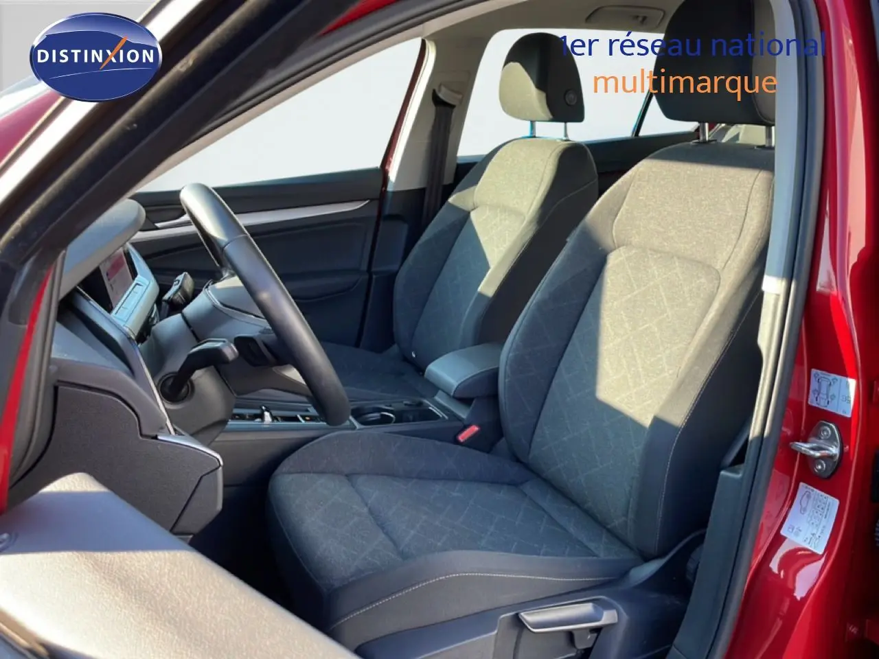 Vue intérieure côté conducteur de la Volkswagen Golf VIII rouge, sièges tissu gris et volant multifonction noir.