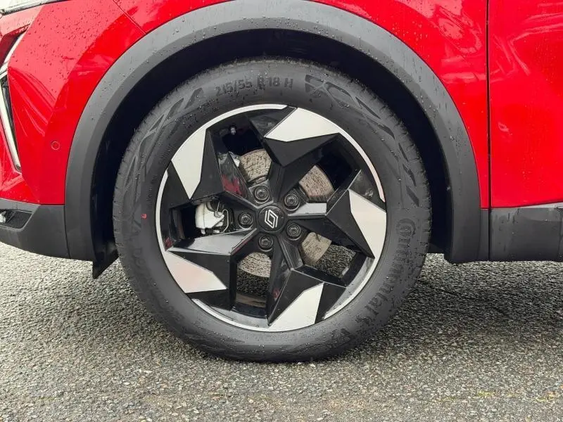 Gros plan sur la roue avant gauche du Renault Captur 2025 rouge Flamme, mettant en valeur la jante noire et argentée au design géométrique.