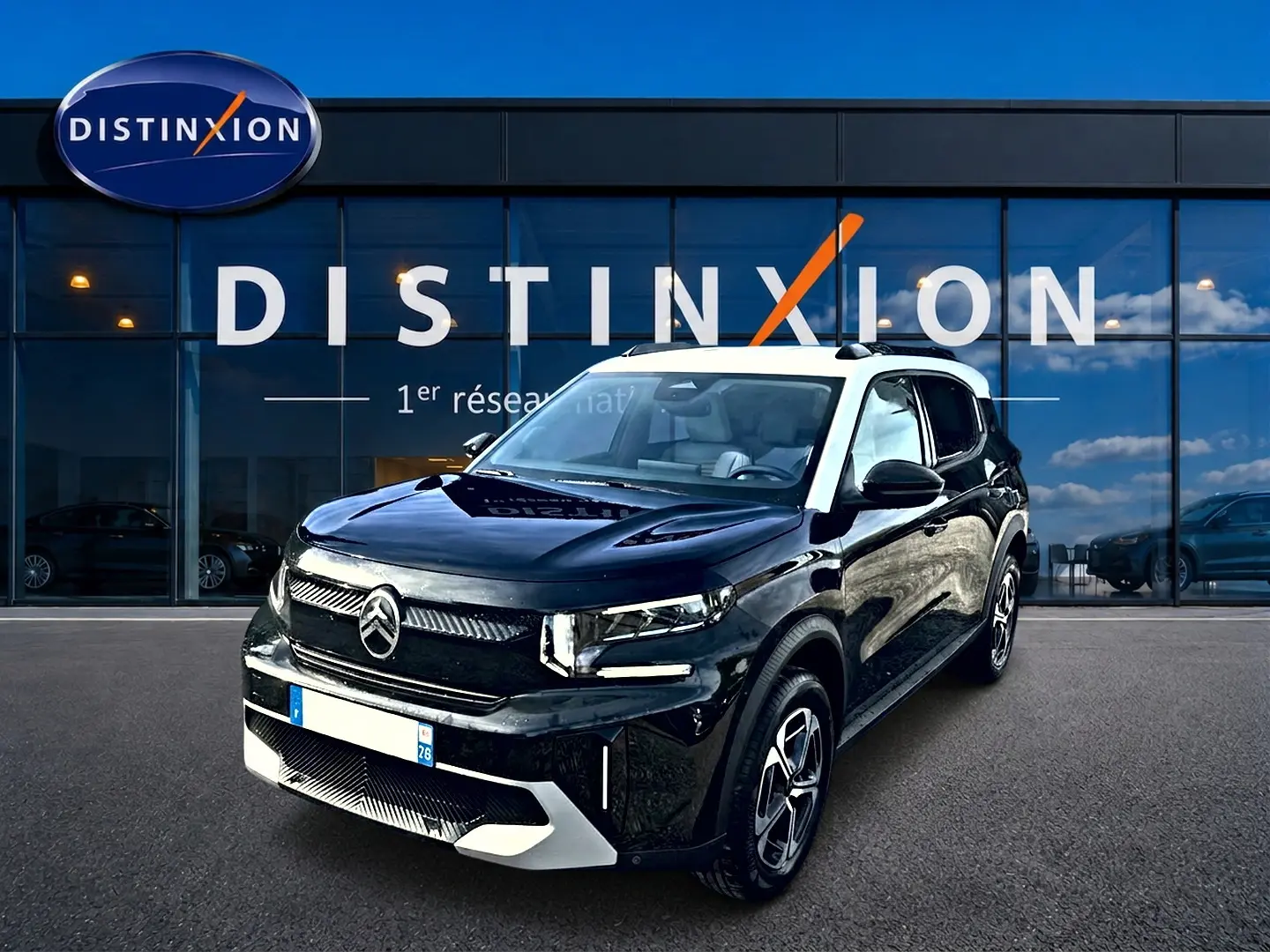 Vue 3/4 avant d'une Citroën C3 Aircross noire avec toit blanc, garée devant une vitrine Distinxion.