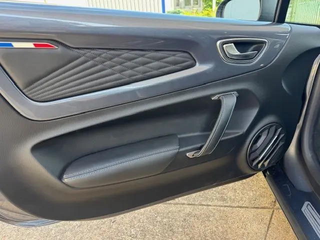 Vue intérieure côté gauche de la porte en cuir noir avec surpiqûres et poignée métallique de l'Alpine A110 Gris Acier Heritage 2021.