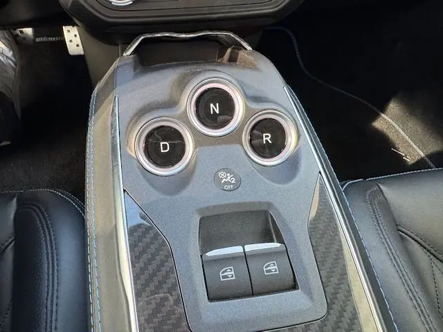 Vue rapprochée de la console centrale en carbone brillant de l'Alpine A110 1.8T 252 Légende avec surpiqûres bleues sur cuir noir.