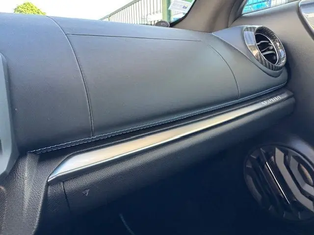 Vue rapprochée de la planche de bord côté passager de l'Alpine A110 gris acier avec surpiqûres bleues et aérateurs ronds chrome.