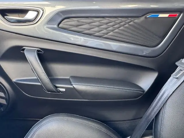 Vue rapprochée de la porte intérieure côté droit de l'Alpine A110 gris acier avec surpiqûres et drapeau tricolore.