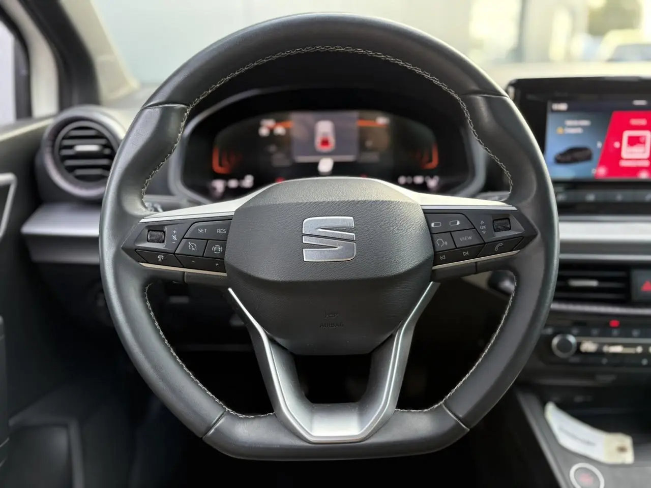 Gros plan sur le volant cuir noir de la SEAT IBIZA TSI 115 Xcellence 2025 avec commandes intégrées et tableau de bord numérique.