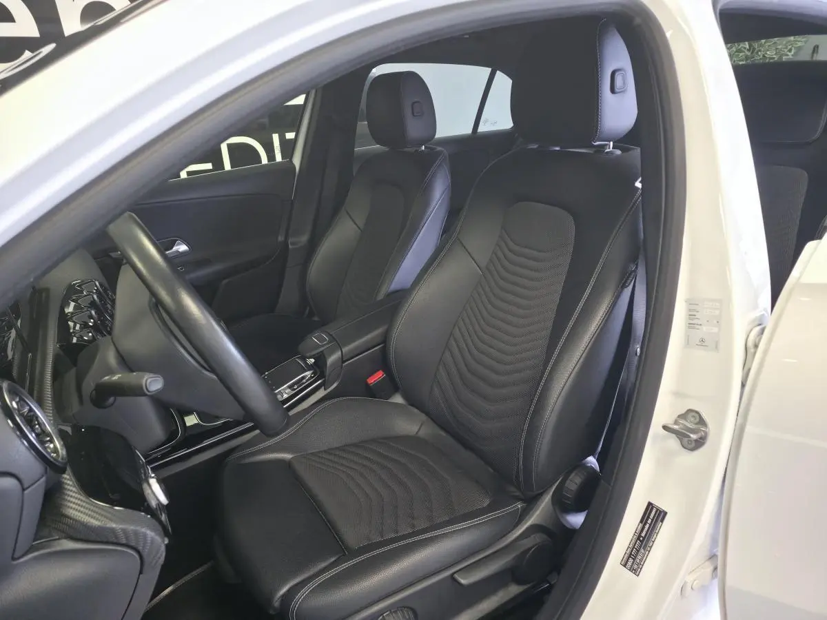 Vue intérieure côté conducteur d'une Mercedes Classe A 160 Style Line blanche avec sièges noirs en tissu et similicuir.
