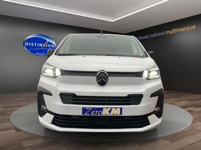 Vue frontale d'un Citroën Jumpy XL blanc 2025 avec phares allumés et plaque "Zéro KM" en showroom.