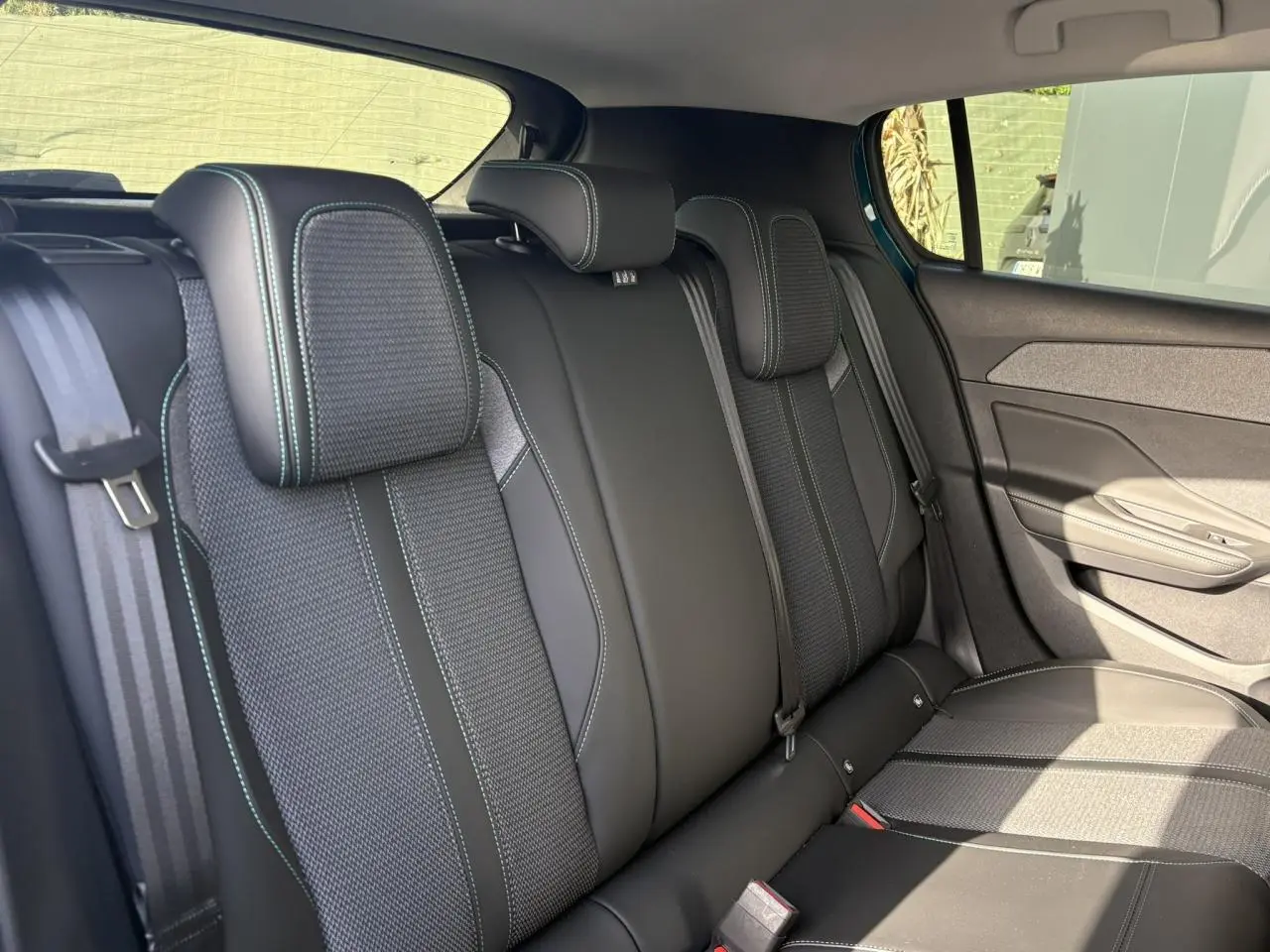 Vue latérale droite des sièges arrière en tissu et cuir noir avec surpiqûres vertes de la Peugeot 308 Hybrid 2025.