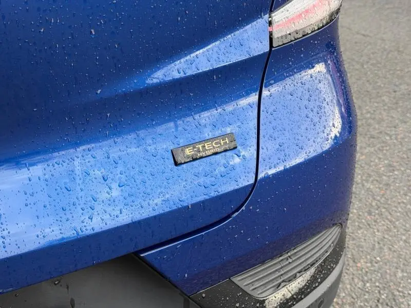 Gros plan sur l'arrière droit bleu Iron d'un Renault Captur 2025 avec badge E-Tech Hybrid sous la pluie.