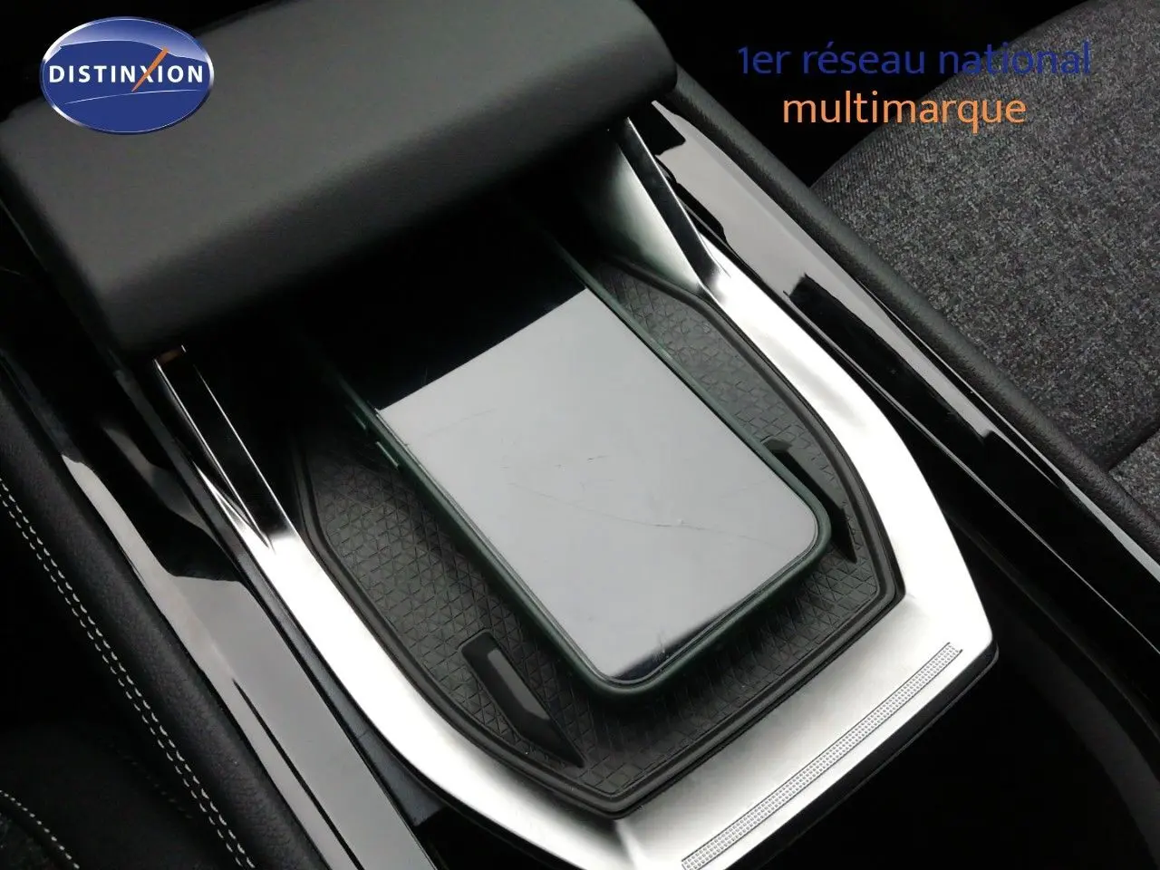 Gros plan sur la console centrale noire et argentée du Renault Austral E-Tech Hybrid avec un smartphone posé dessus.