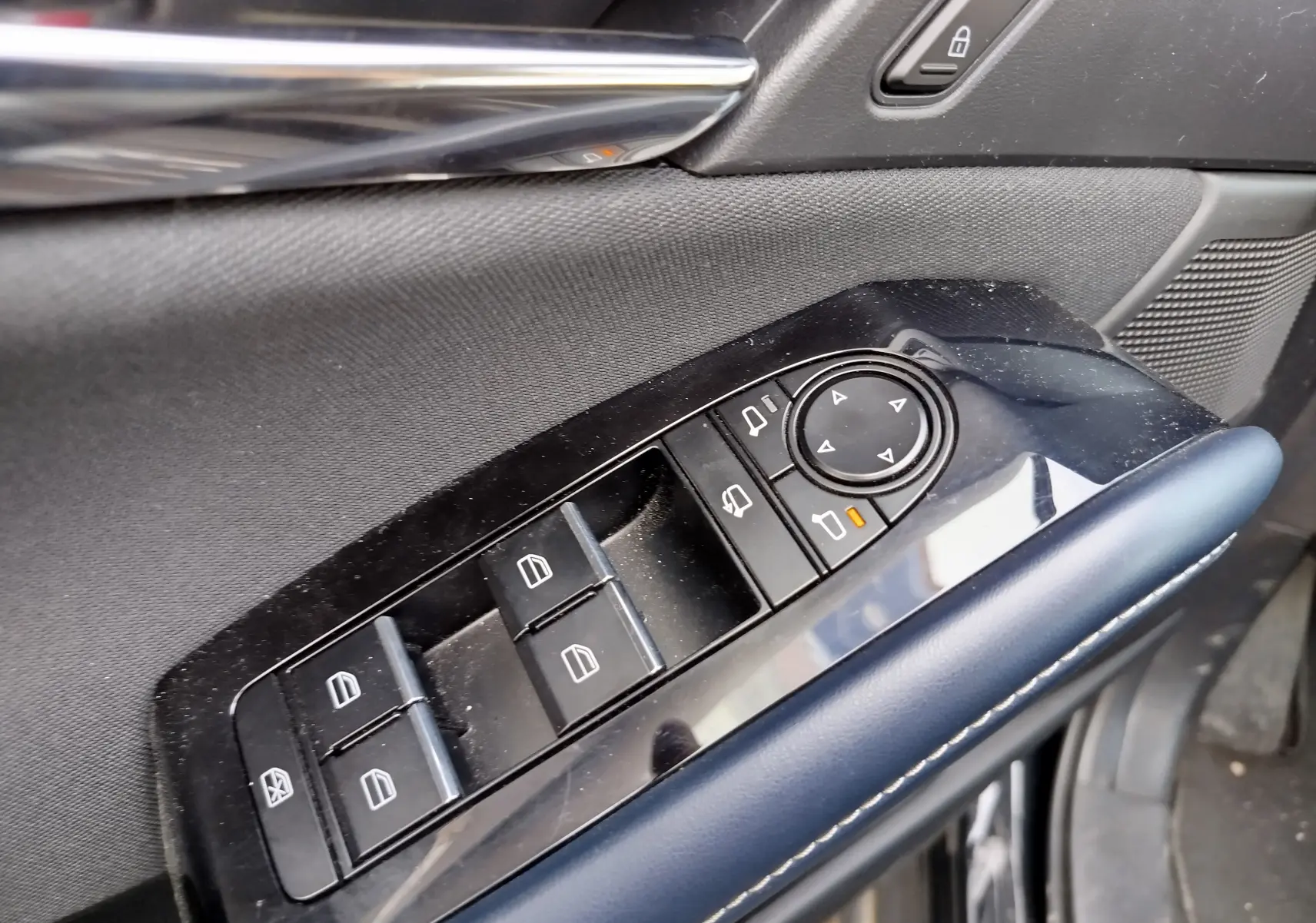Gros plan sur les commandes des vitres et rétroviseurs côté conducteur du Mazda CX-30 noir, avec accoudoir en cuir bleu.