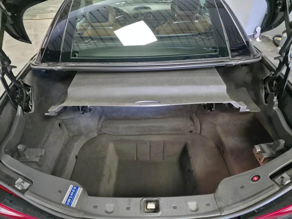 Coffre ouvert vu de l'arrière d'une Mercedes SL 500 noire, avec intérieur de coffre en tissu gris.