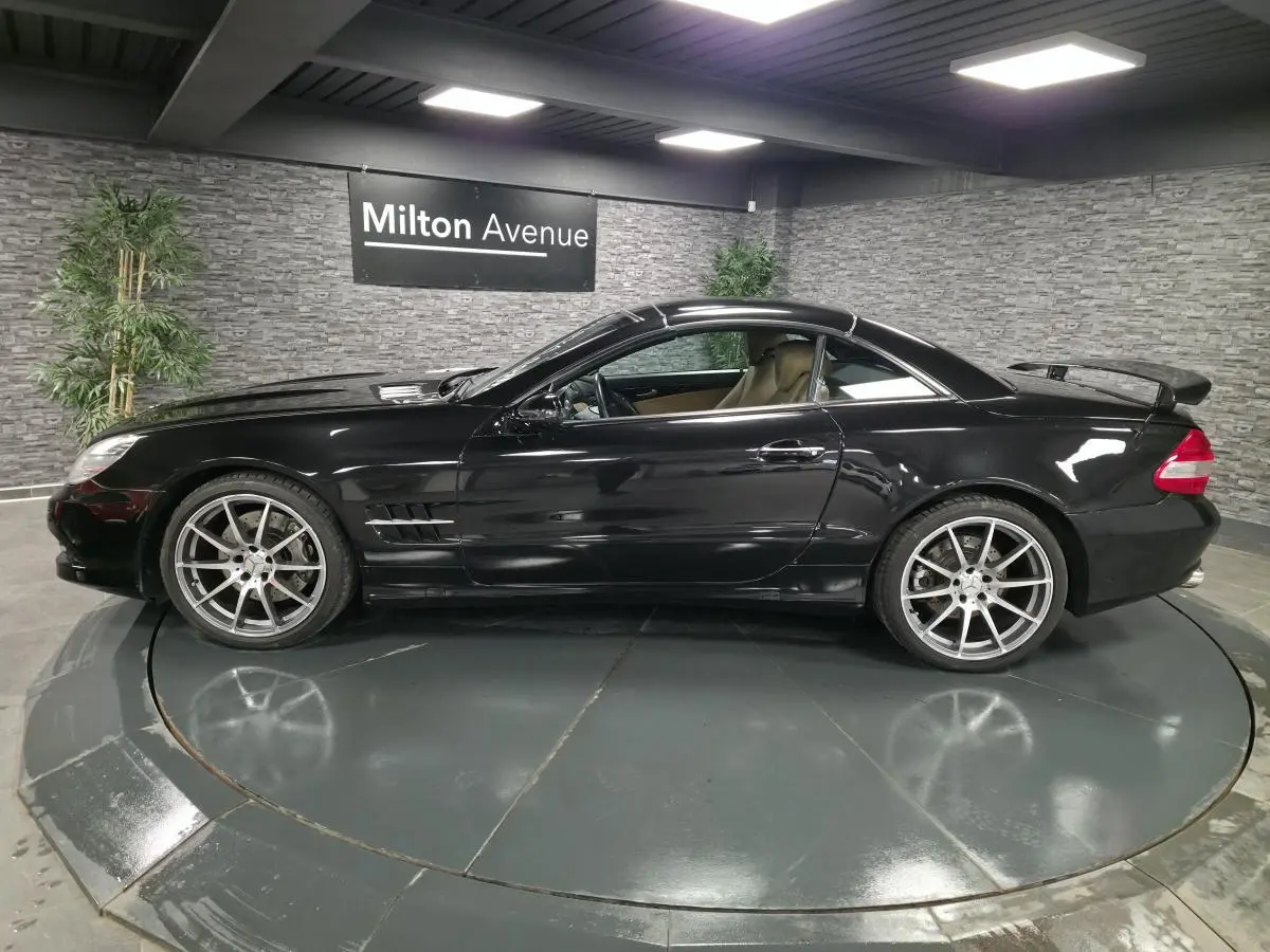 Profil côté gauche d'une Mercedes SL 500 noire avec jantes alliage 19 pouces et aileron arrière en intérieur showroom.
