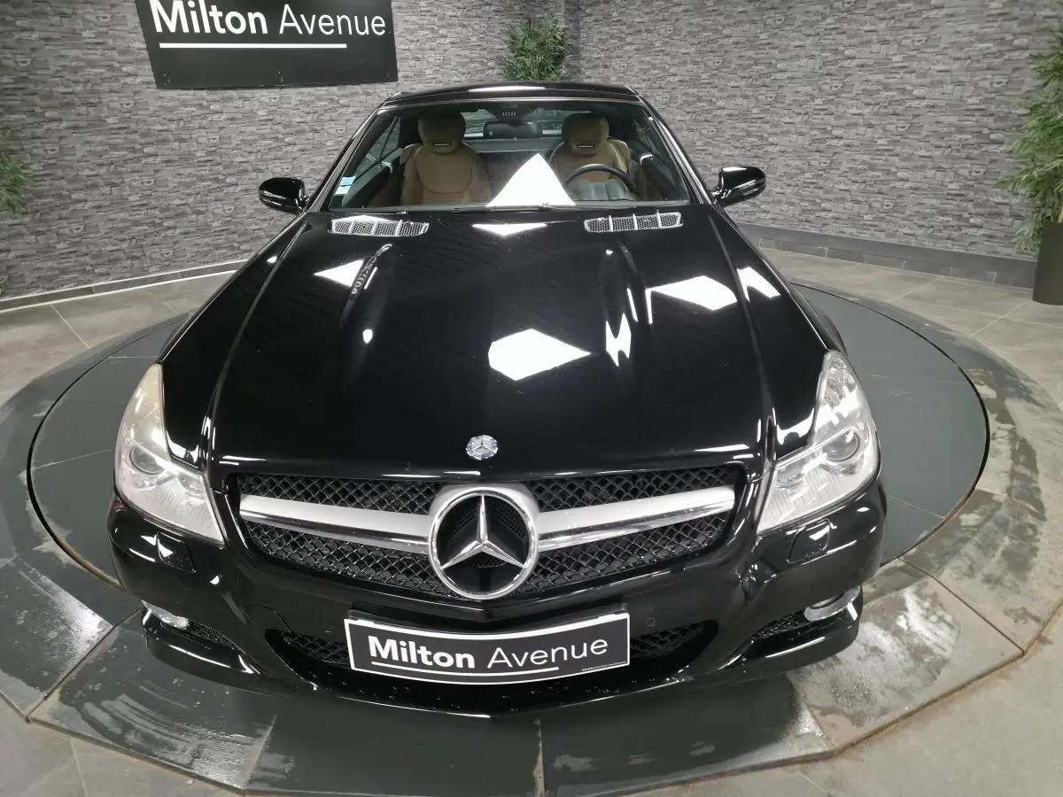 Vue avant plongeante d'une Mercedes SL 500 noire avec calandre AMG et intérieur cuir beige visible.