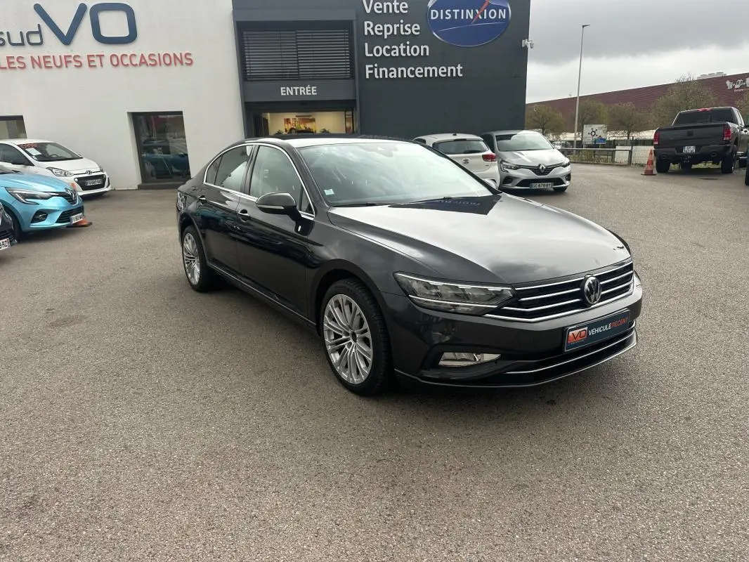 Volkswagen Passat gris foncé vue 3/4 avant droit sur parking devant concession automobile.