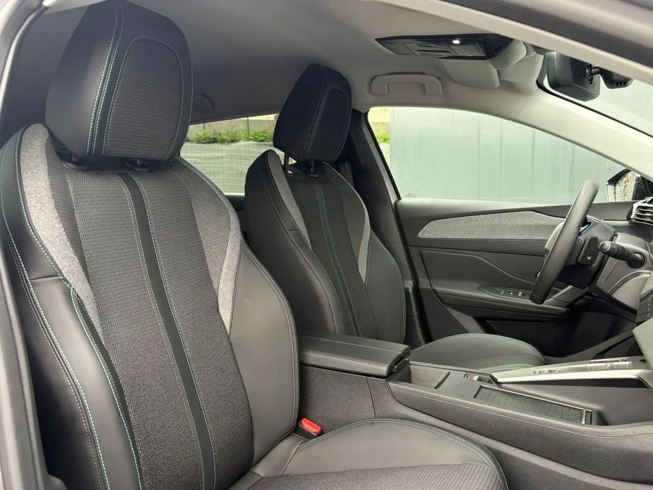 Vue intérieure côté conducteur de la Peugeot 308 SW Hybrid 145, sièges tissu et cuir noir avec surpiqûres vertes.