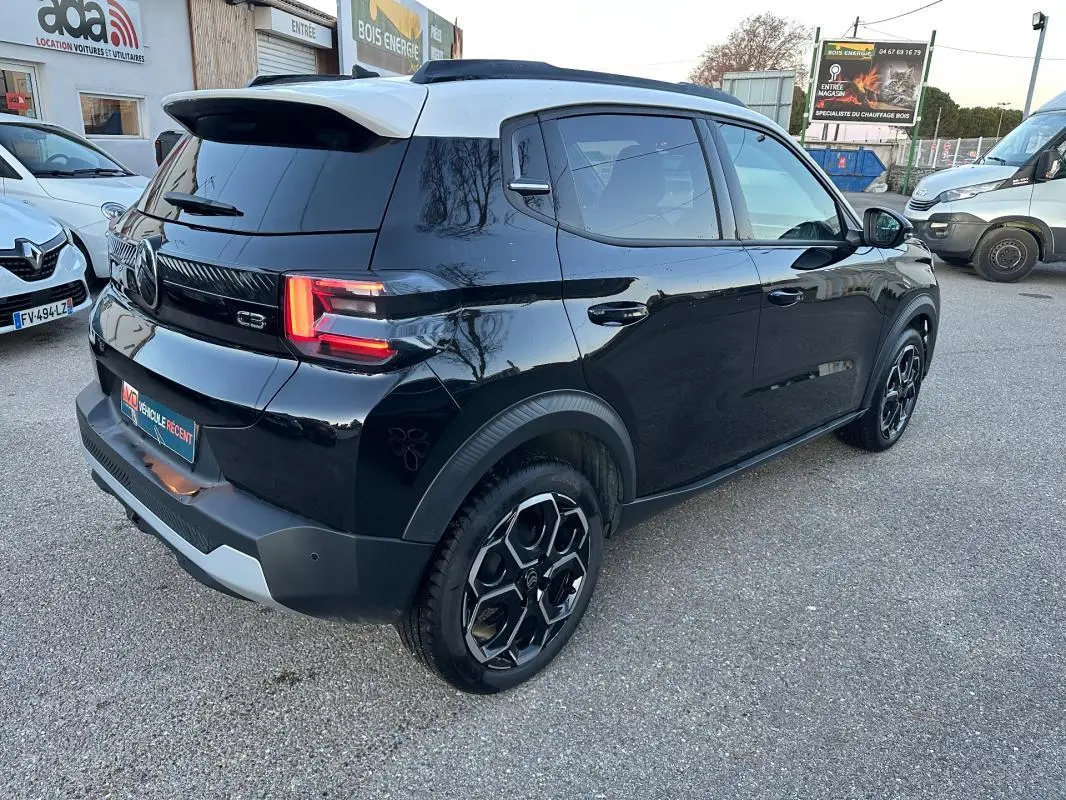 Vue 3/4 arrière droite d'une Citroën C3 noire 2025 avec jantes alliage 17 pouces et barres de toit visibles.