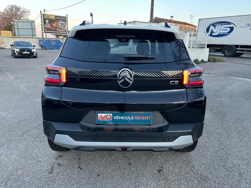 Vue arrière d'une Citroën C3 noire 2025 avec barres de toit et jantes alliage 17 pouces sur parking.