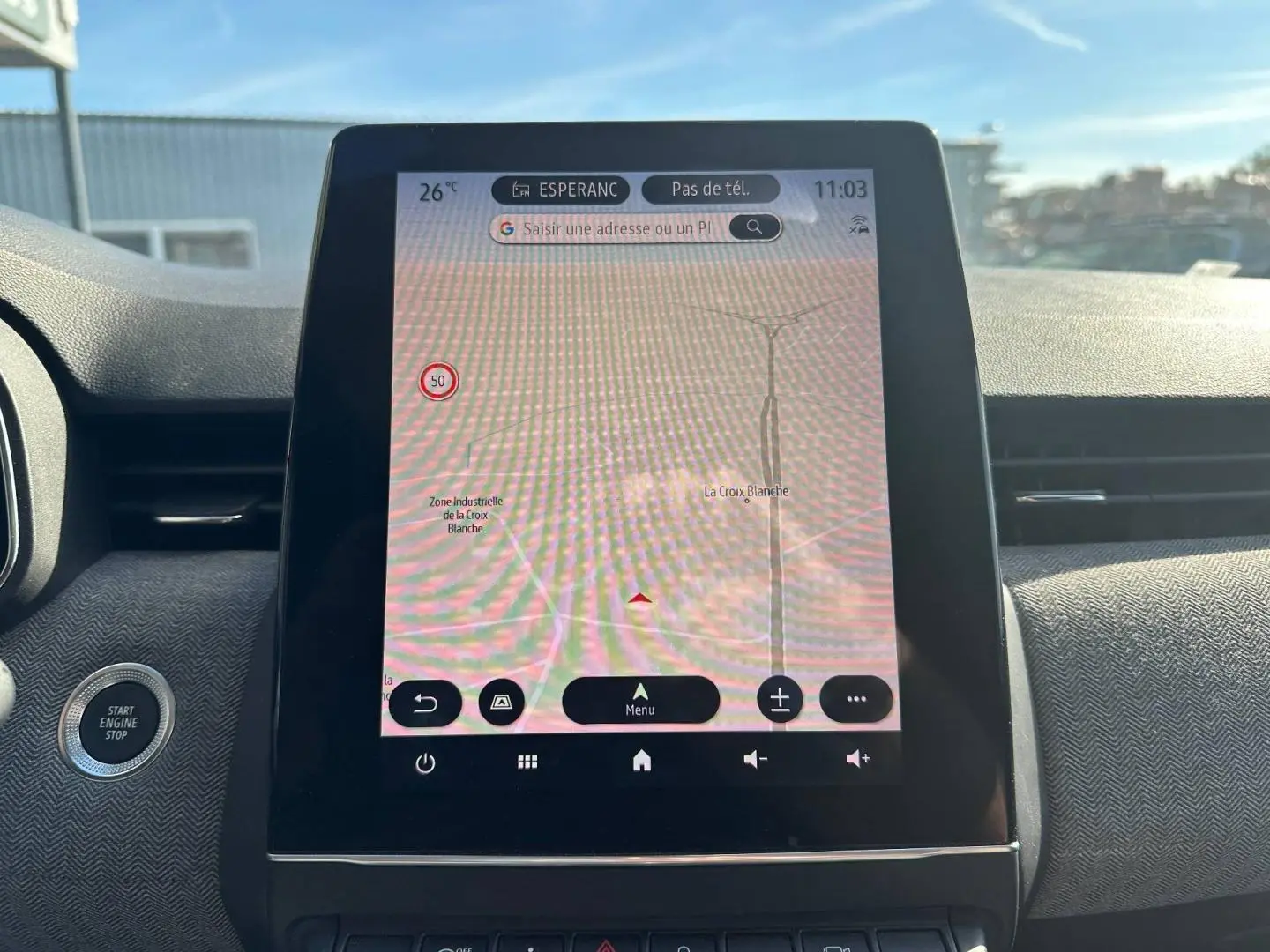 Vue intérieure centrée sur l’écran tactile GPS de la Renault Clio rouge flamme, avec bouton démarrage à gauche visible.